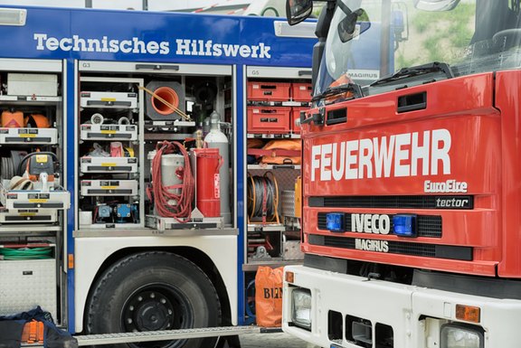 Auf dem Bild sind ein geöffneter Wagen vom THW mit vielen Materialien darin zu sehen sowie die Frontpartie eines Feuerwehrautos.