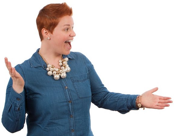 Eine Frau mit kürzeren roten Haaren schaut nach rechts, öffnet Ihre Arme und scheint sich über etwas sehr zu freuen.