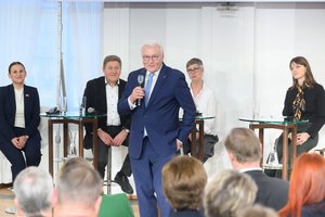 Bundespräsident Steinmeier mit Mikro in der Hand spricht zum Publikum, 4 Diskutant*innen sitzen im Hintergrund auf Bistristühlen.