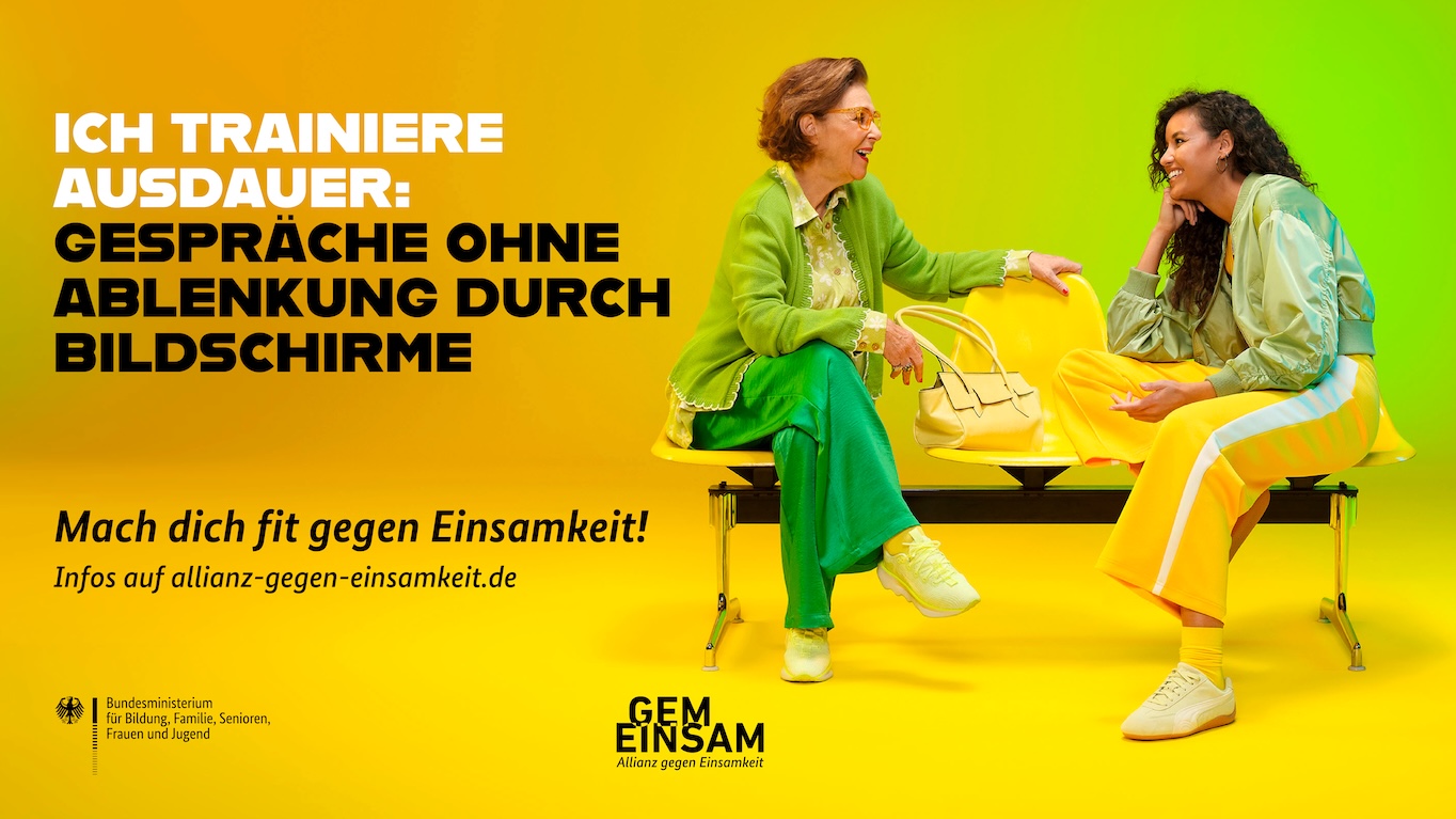 Zwei bunt gekleidete Frauen sitzen auf einer Bank und unterhalten sich angeregt.