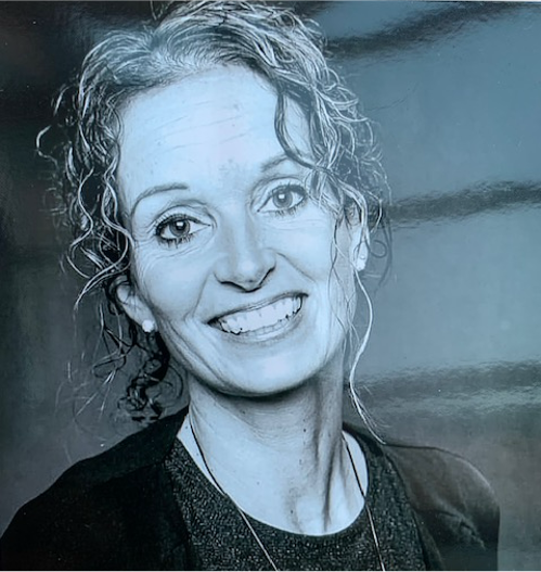 auf diesem schwarz-weiß Foto ist der Kopf einer in die Kamera lächelnden Frau zu sehen, deren gewelltes Haar locker fällt.